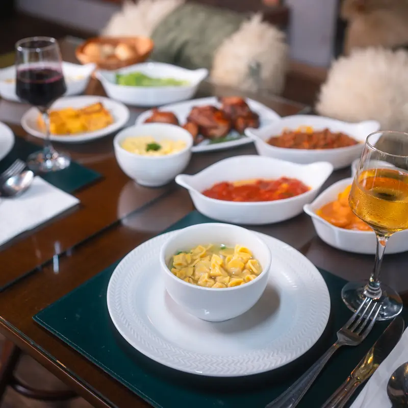 Sopa de capeletti servida à mesa posta, com a sequência ao fundo