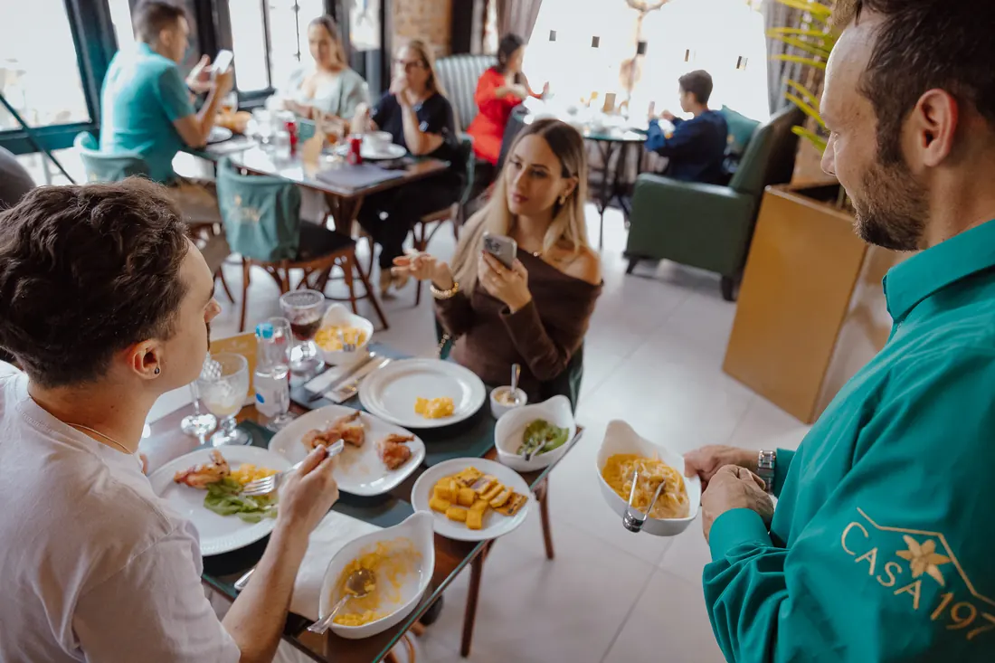 Atendente servindo massa à mesa durante o almoço na Casa 197